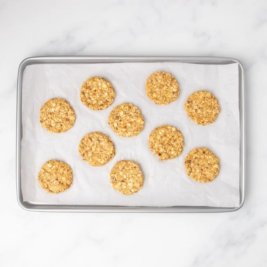 10 evenly spaced round raw cookie disks on white paper on baking tray