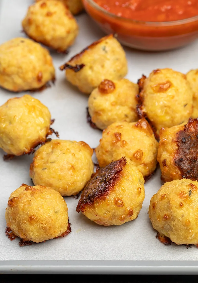 12 baked chicken meatballs on white paper on tray with small bowl of red tomato sauce