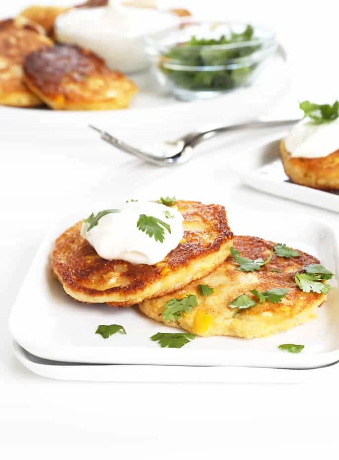 2 corn cakes on a white plate with sour cream and herbs on top 