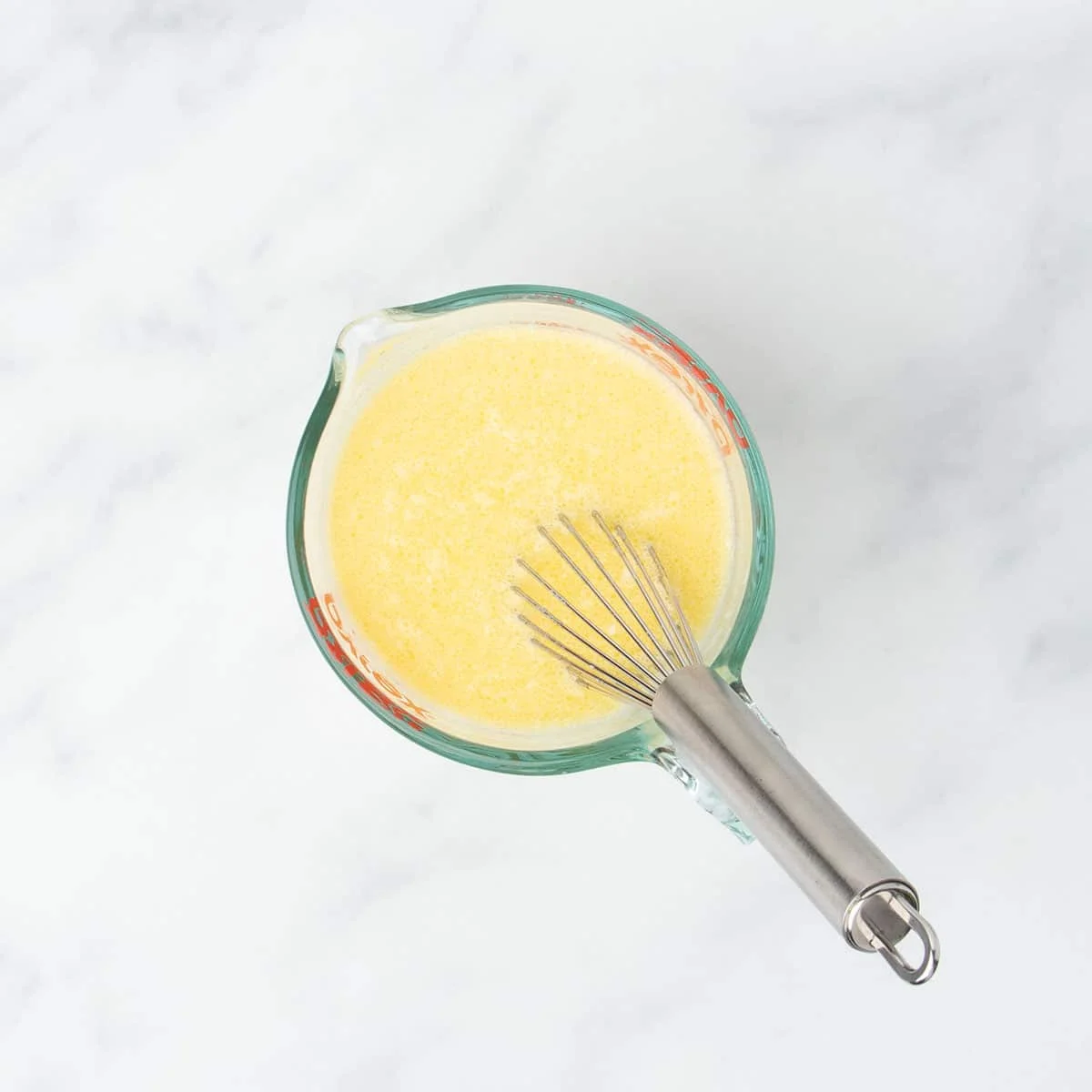 2 cup glass measuring cup with yellow whisked mixture and metal wire whisk in cup
