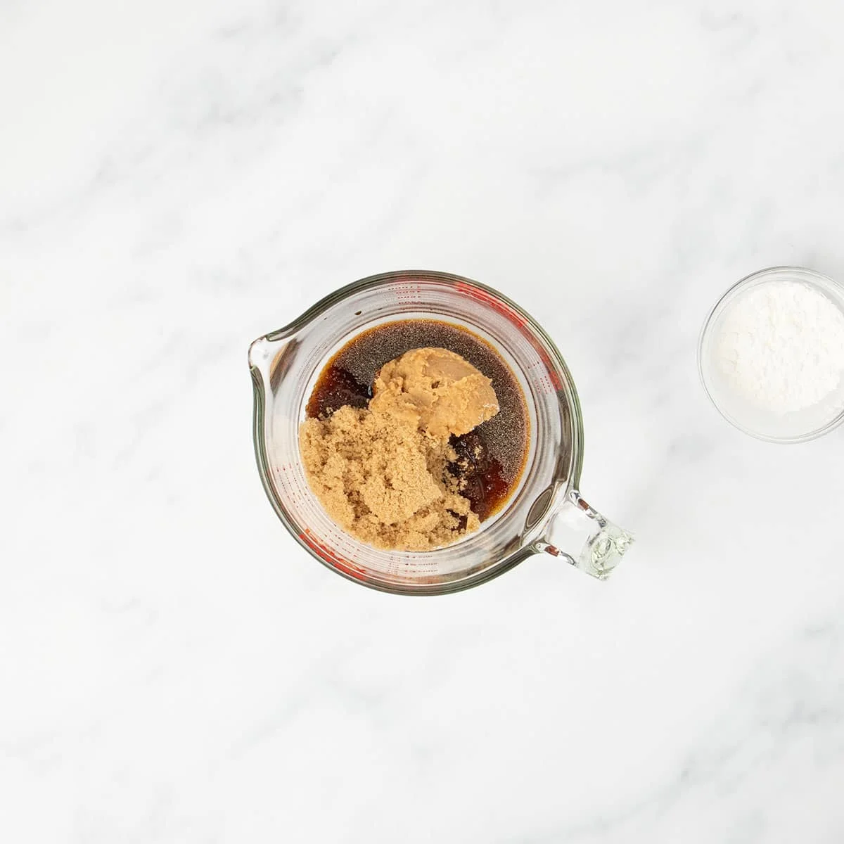 2 cup pyrex measuring cup with brown liquid, powdered spices, and brown sugar