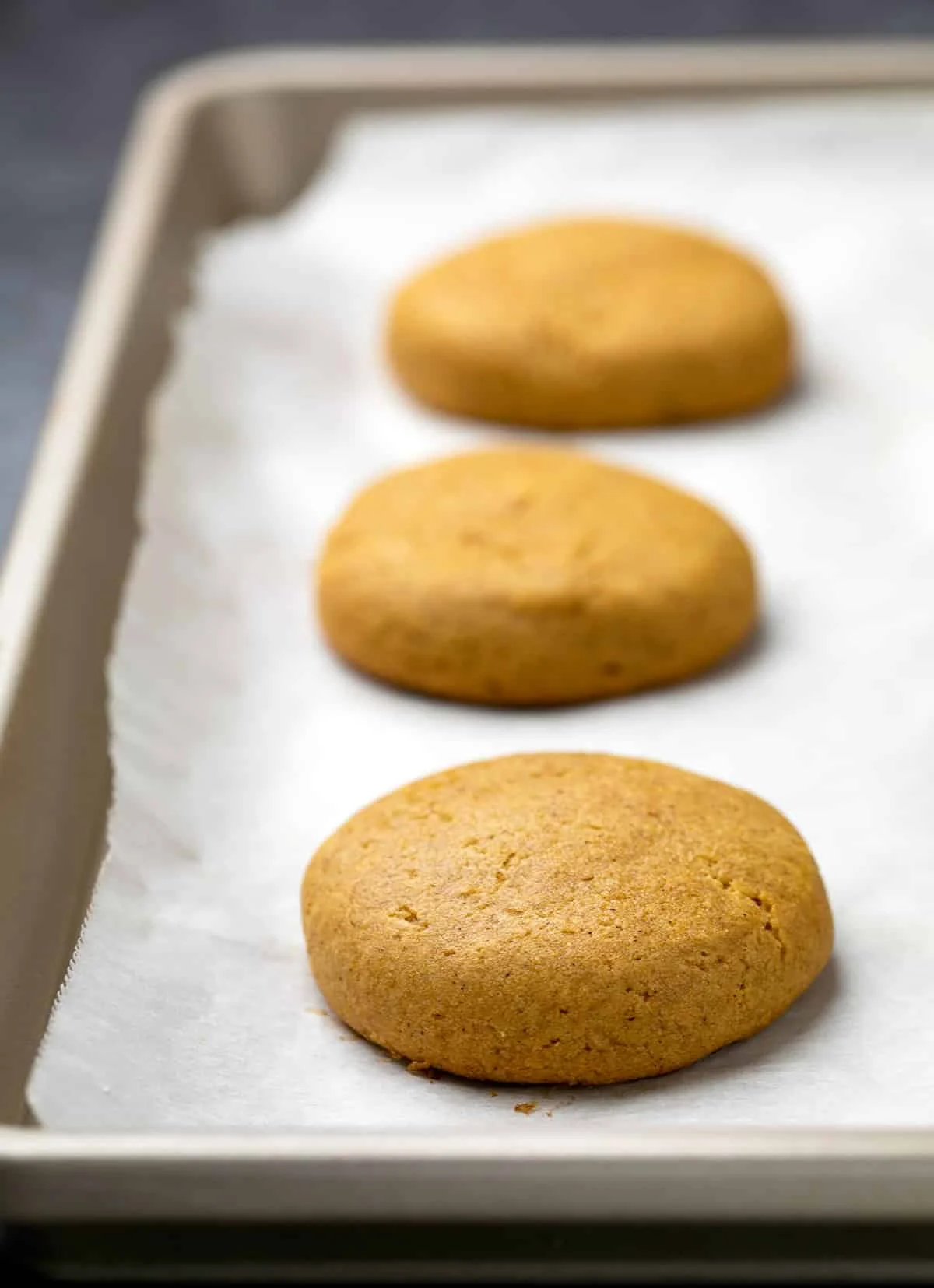 3 baked pumpkin cookies on white paper on tray.