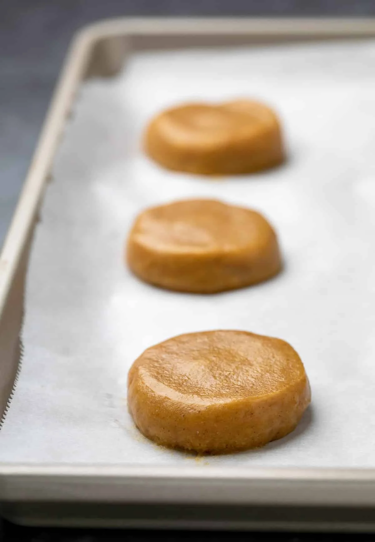 3 disks of raw pumpkin cookie batter on white paper on tray.