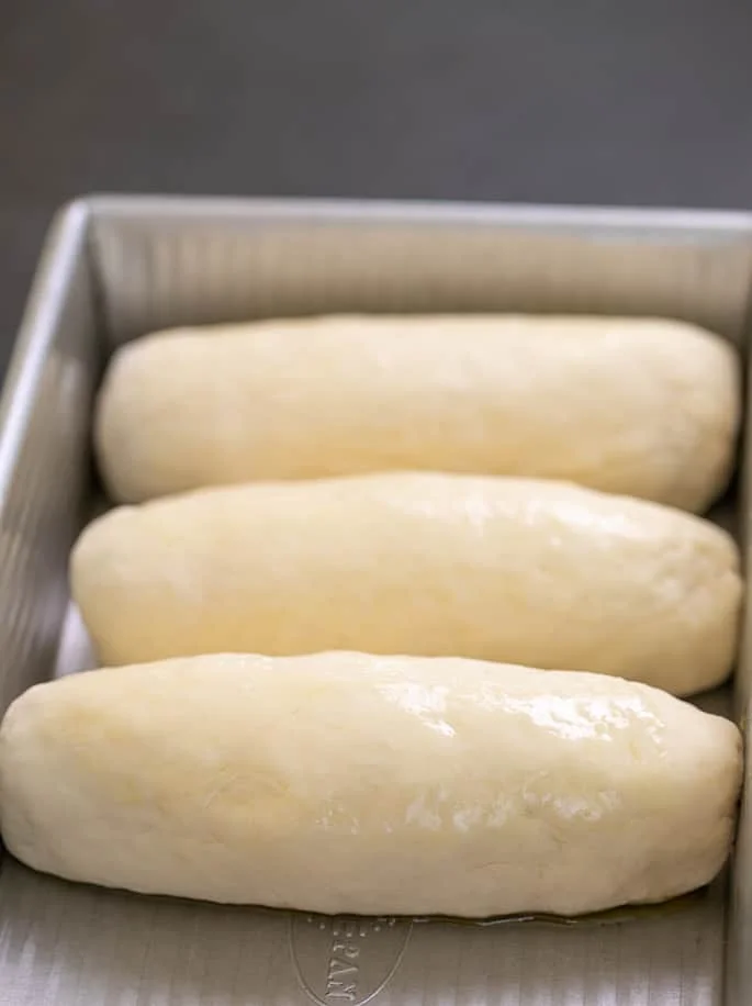 3 raw buns in rectangular metal baking pan.
