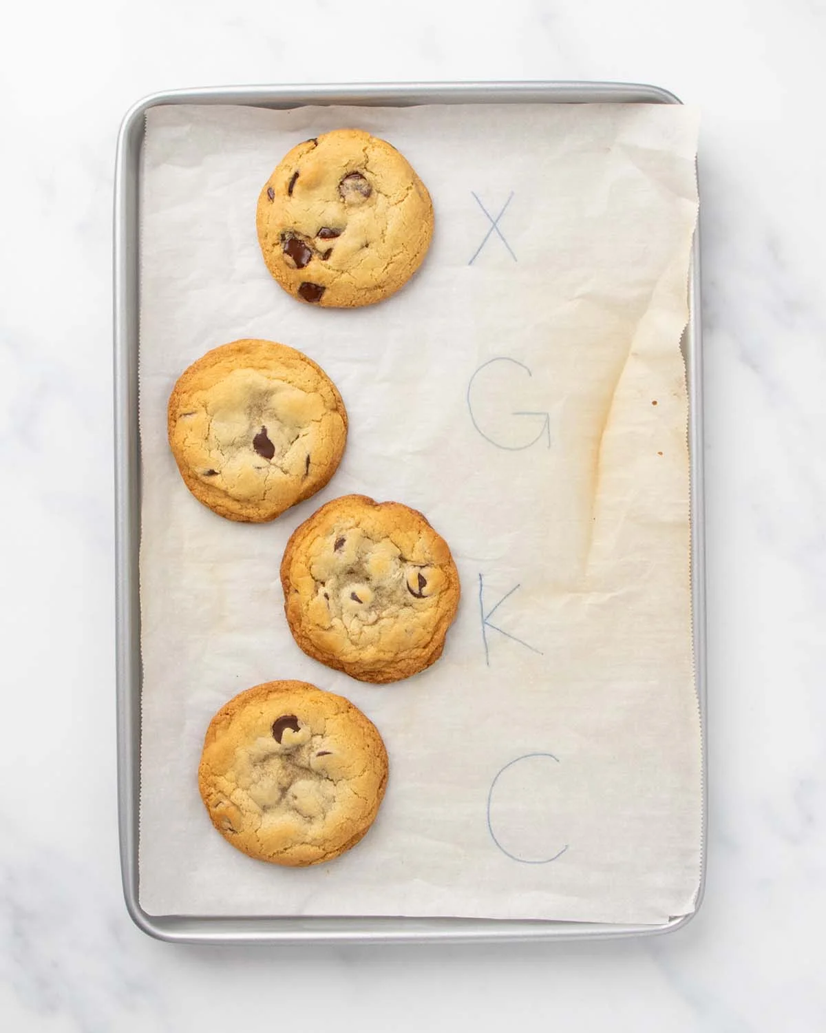 4 baked chocolate chip cookies on white parchment on baking sheet next to letters