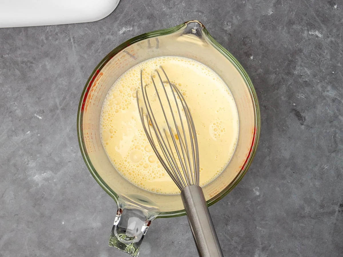 4 cup glass measuring cup with light yellow liquid and metal wire whisk