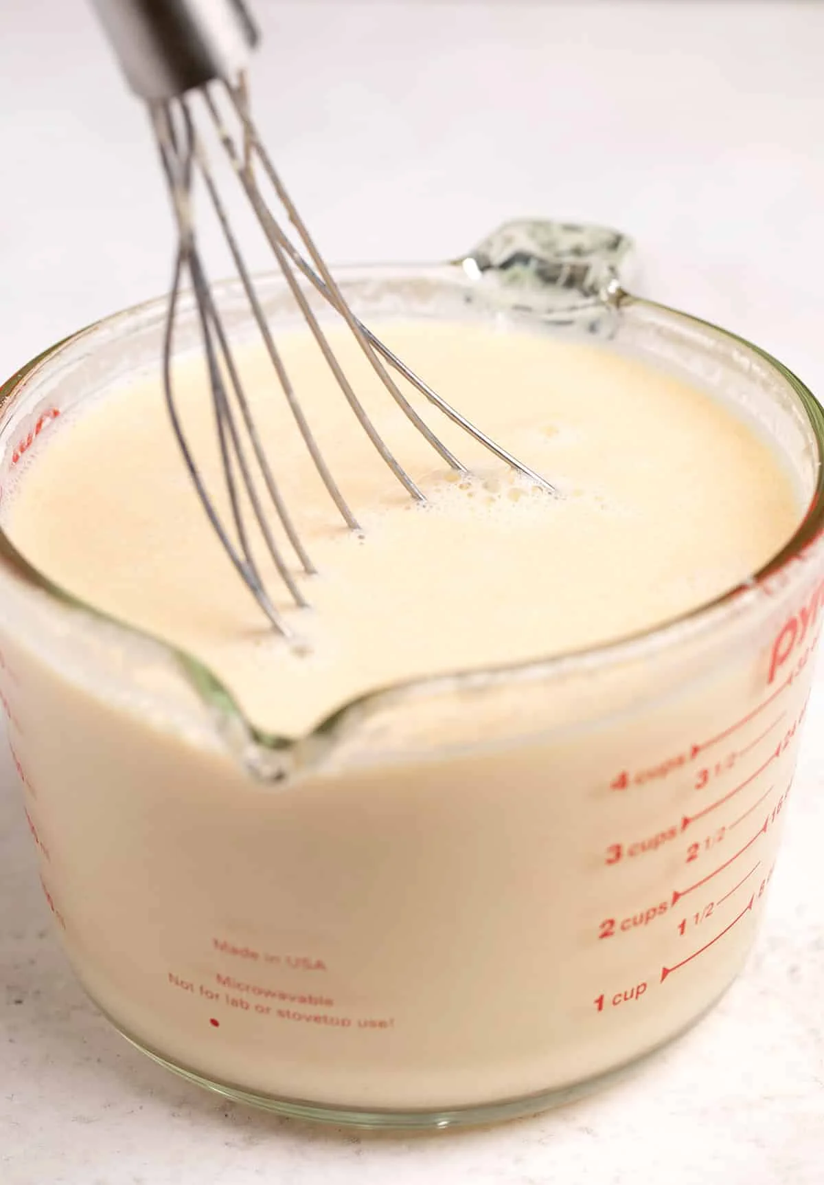 4 cup pyrex measuring cup filled with tan liquid with a flat whisk on white table