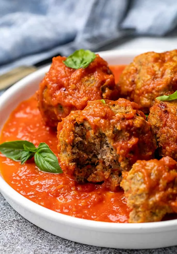 4 meatballs in marinara sauce with one meatball missing a piece