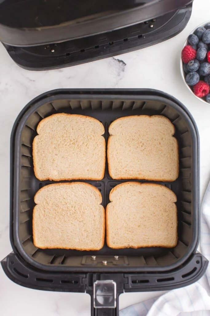 4 pieces of bread in an air fryer basket about to be toasted. 