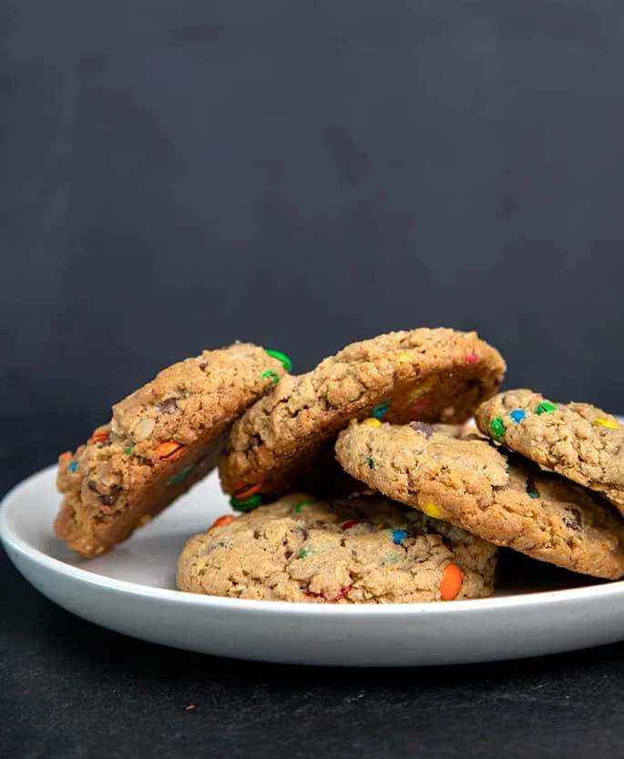 5 light brown cookies with colored candy pieces on round white plate on black surface