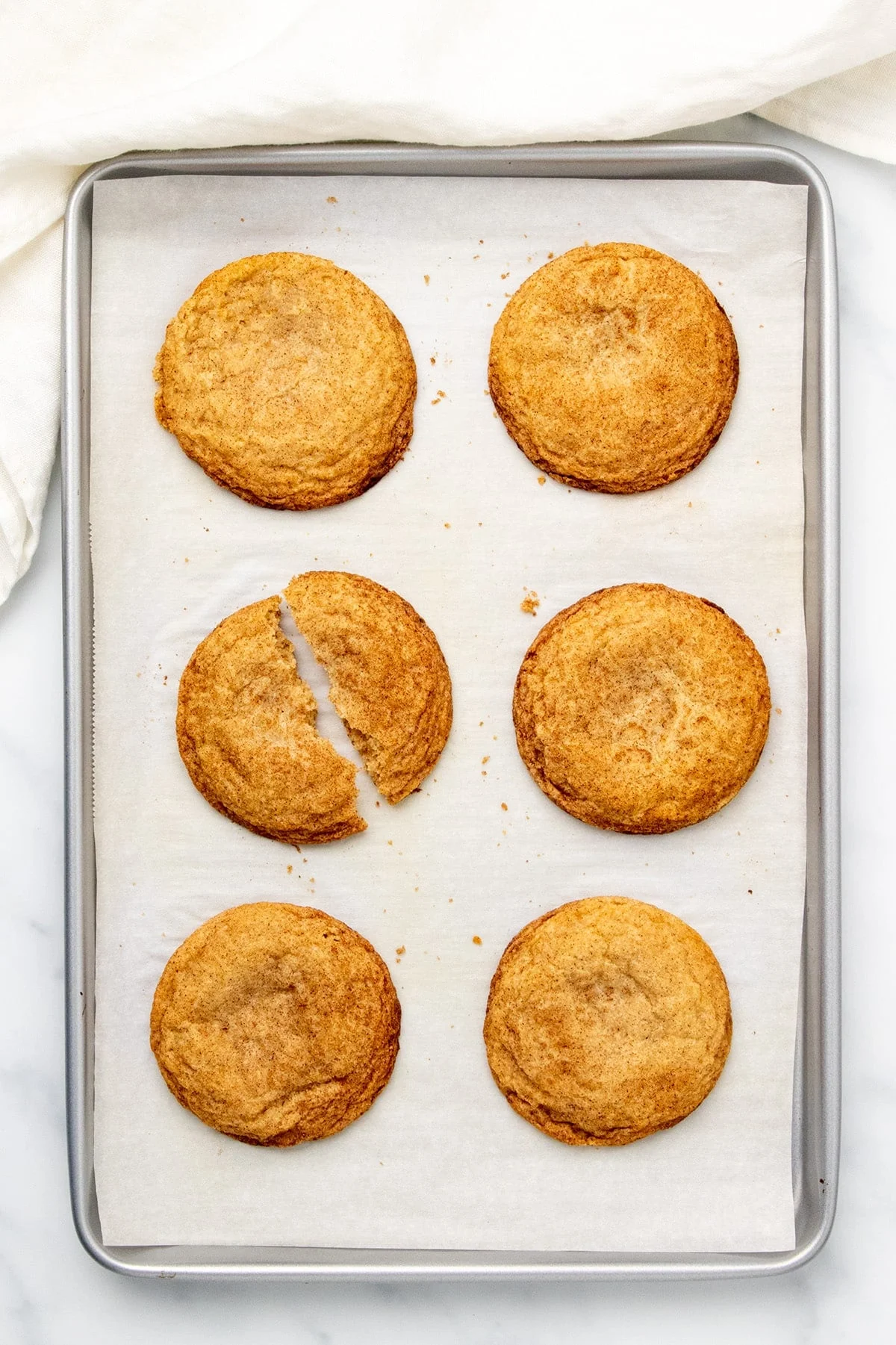 6 large, golden brown snickerdoodles, with one cookie broken in half. 