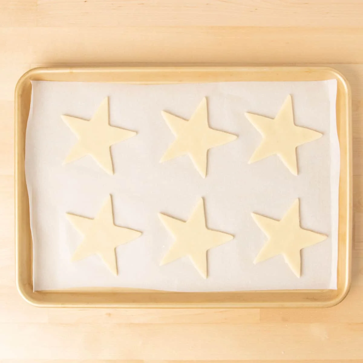 6 star shaped raw cookies on white paper on gold baking sheet