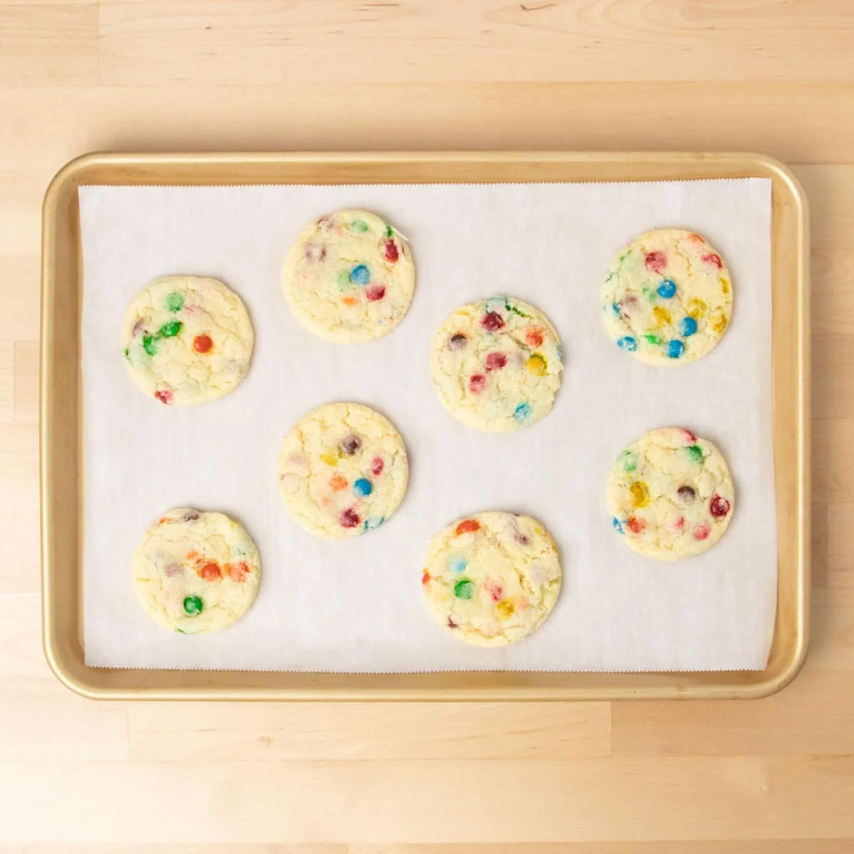 8 baked light yellow cookies with colored candy pieces on baking tray.