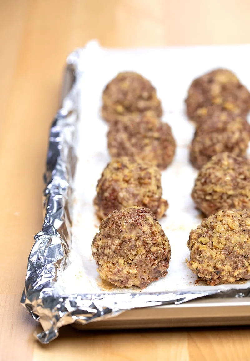 8 baked meatballs on white paper on foil-lined baking tray
