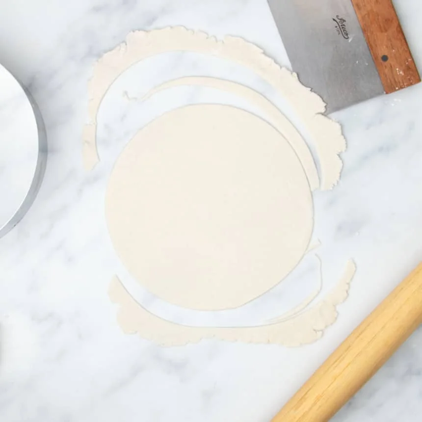 8-inch clean round of dough cut into rolled out raw tortilla dough with dough scraps next to round