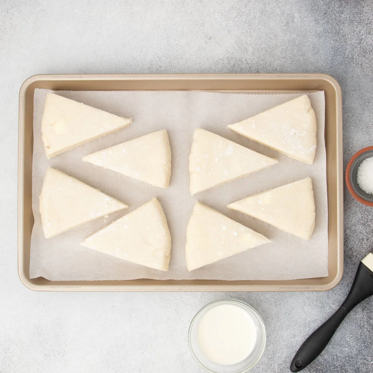 8 raw dough triangles on parchment paper on gold colored rimmed baking sheet.