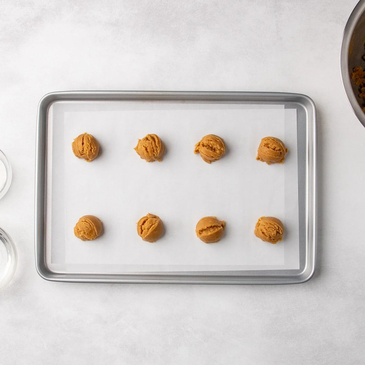 8 scoops of peanut butter cookie dough arranged in rows on a parchment-lined baking sheet.