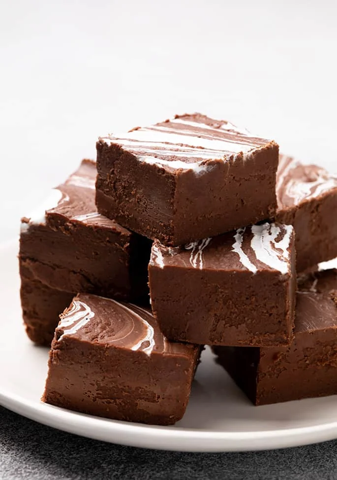 8 squares of brown fudge with white swirl on top arranged in stacked layers on small white plate