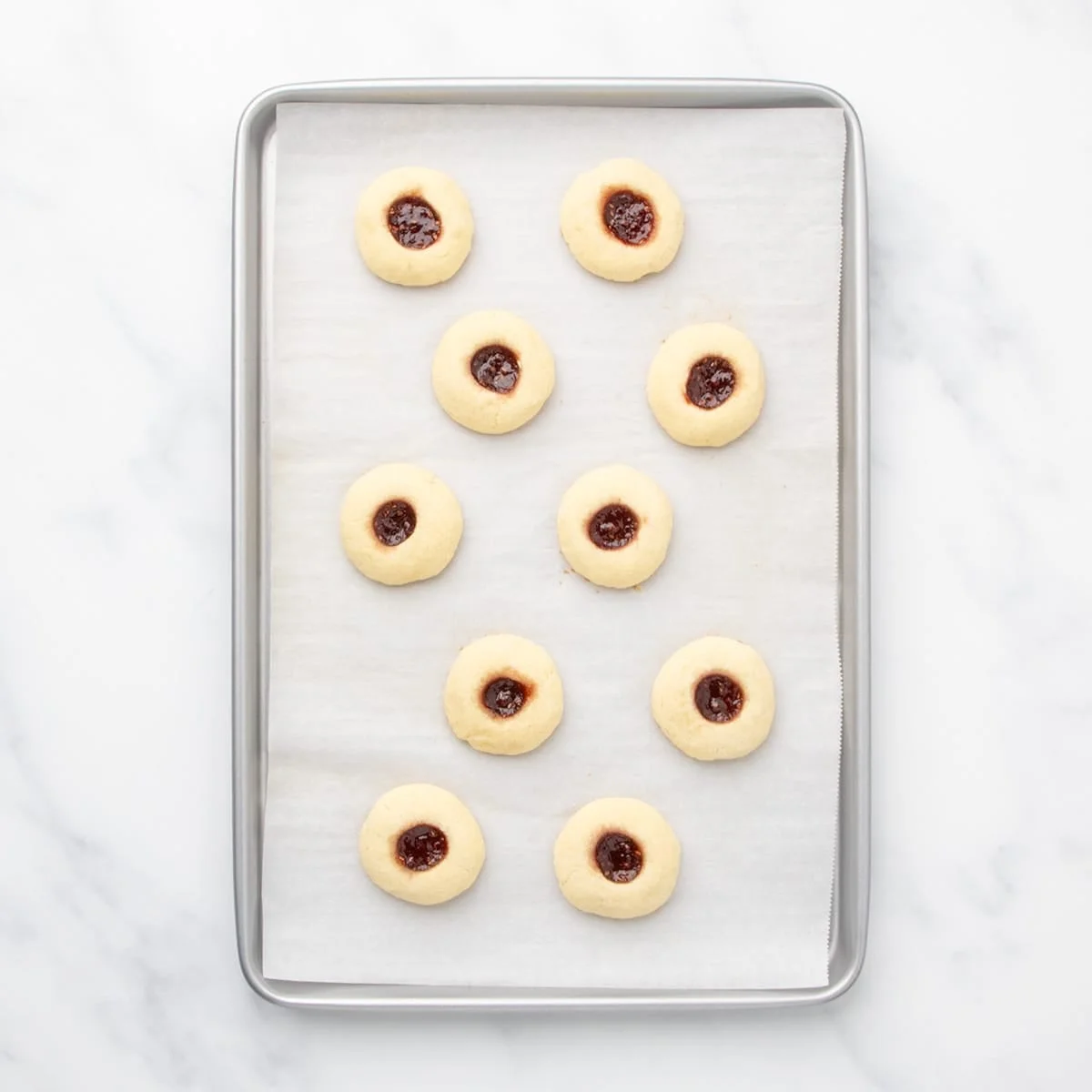 A baking sheet lined with parchment paper holding baked cookies with jam centers.