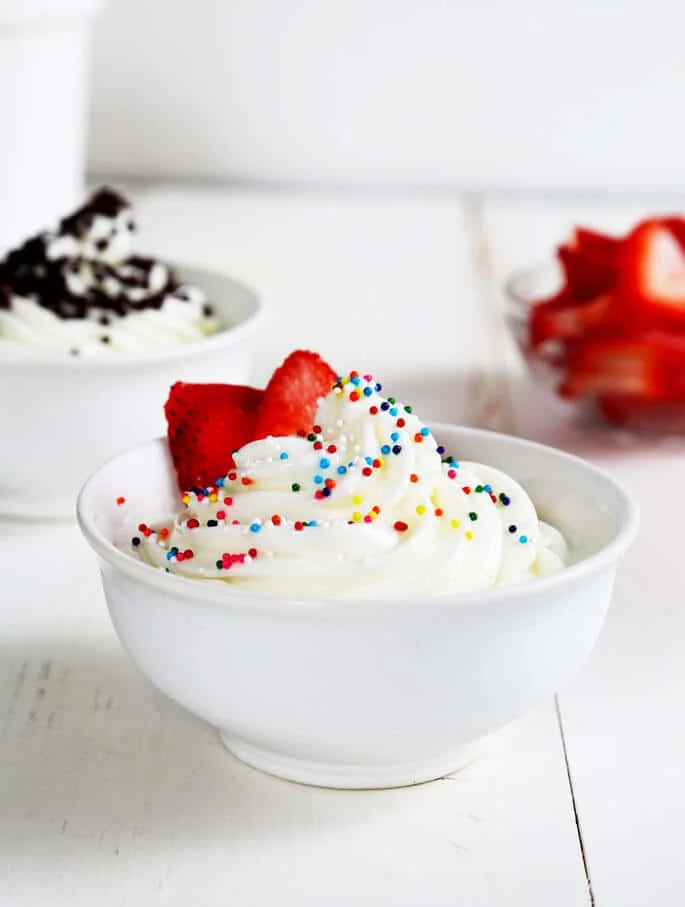 A bowl of frozen yogurt with nonpareils and strawberries on top
