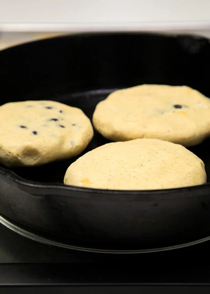 A cast iron skillet with raw black bean pupusas