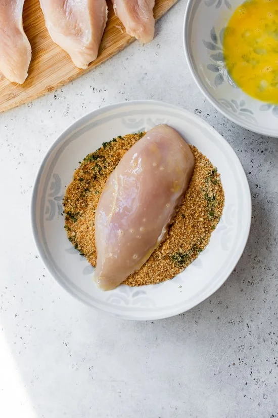 A chicken breast in a bowl of breading