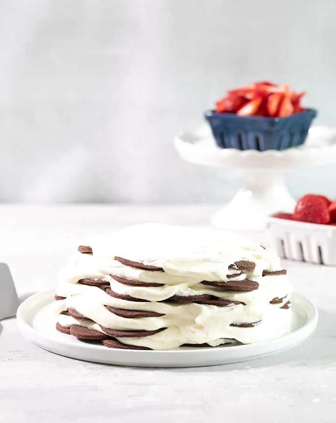A chocolate wafer cookie icebox cake on a platter with berries in the background