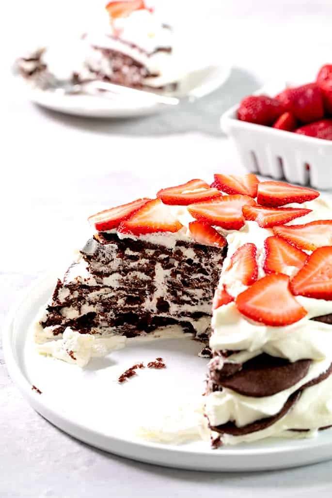 A chocolate wafer cookie icebox cake on a platter with two pieces taken