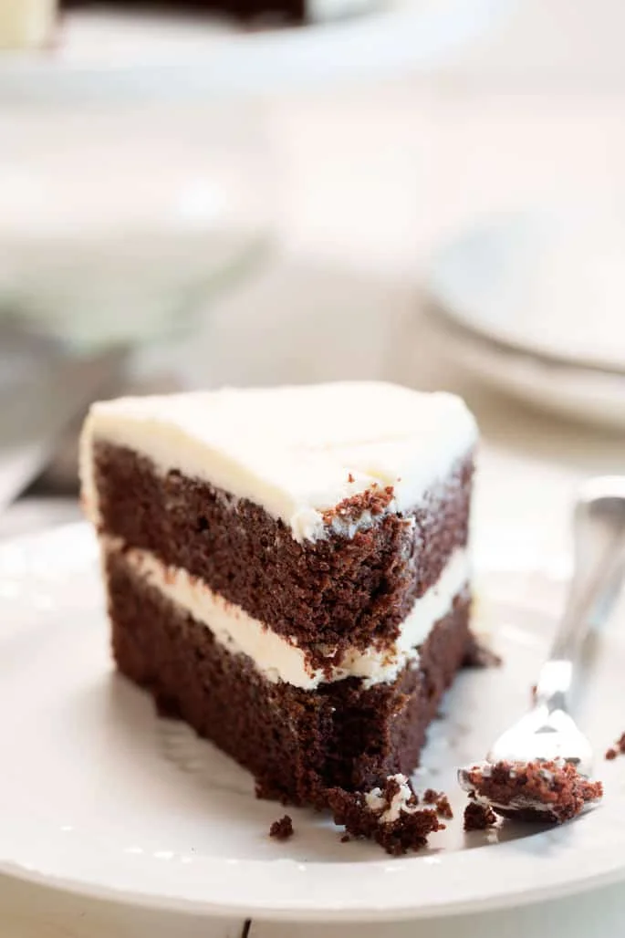 A close up of a piece of devils food cake with bite out of it on white plate and fork