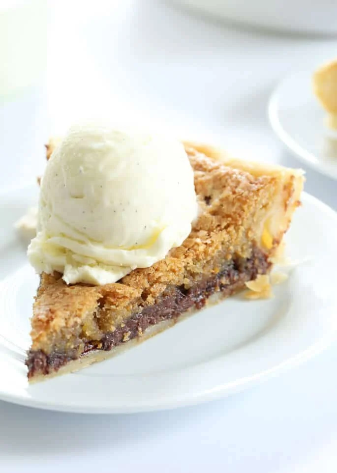 A close up of a slice off chocolate chip pie with a scoop of ice cream on top.