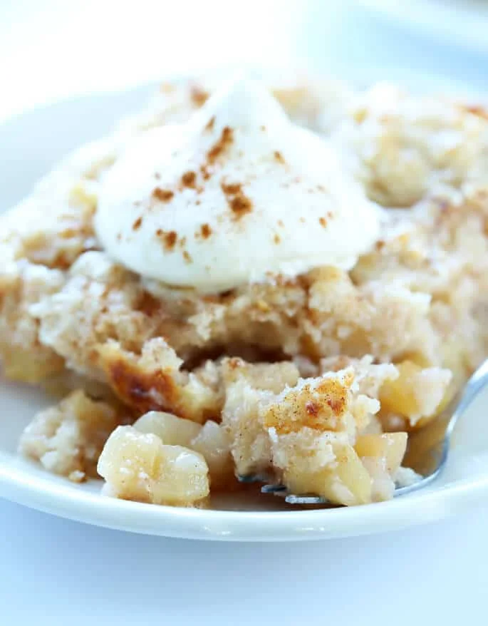 A close up of apple "dump" cake on a plate with whip cream