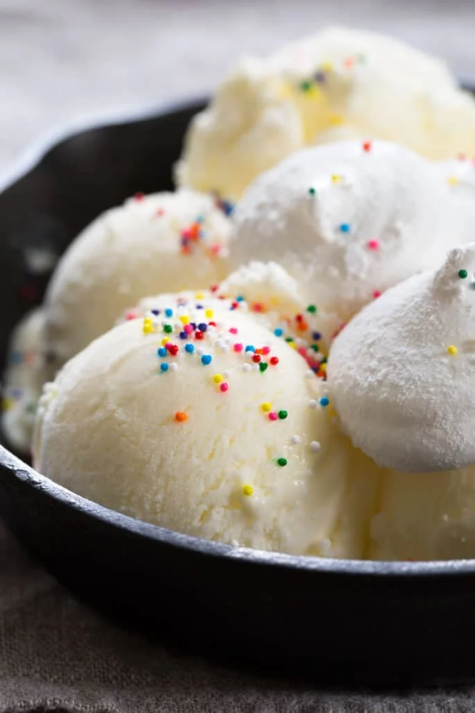 A close up of ice cream with rainbow nonpareils and marshmallows on black skillet
