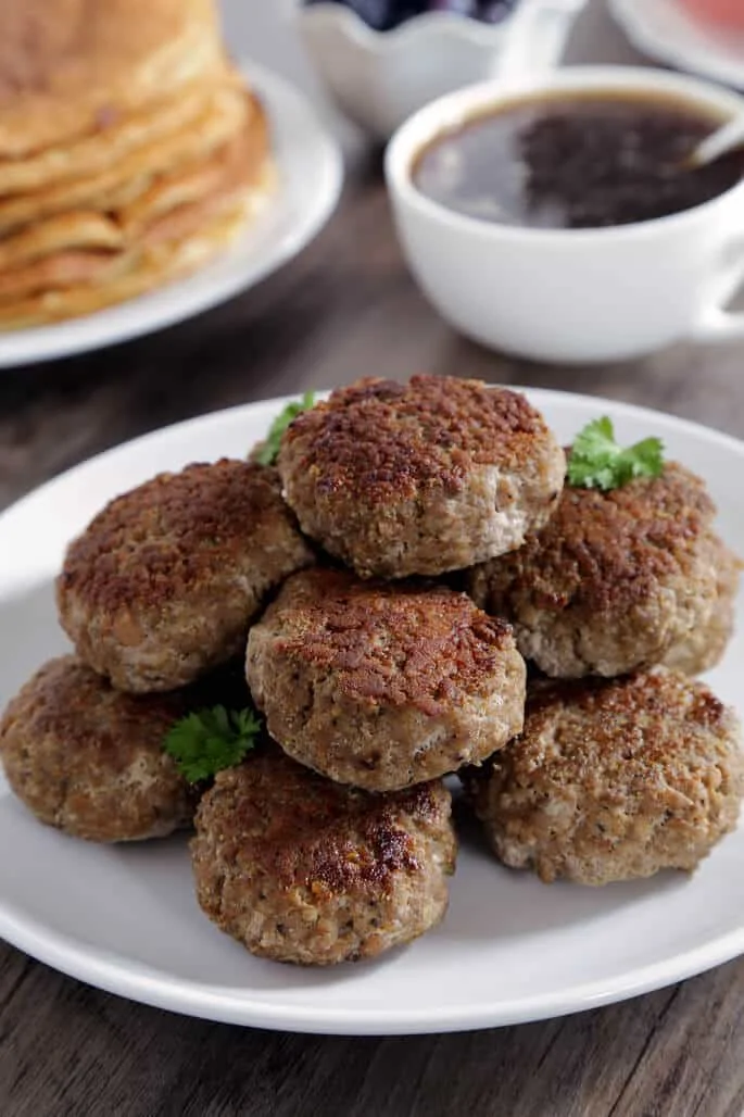 A close up of sausages with herbs on top on a white plate. 