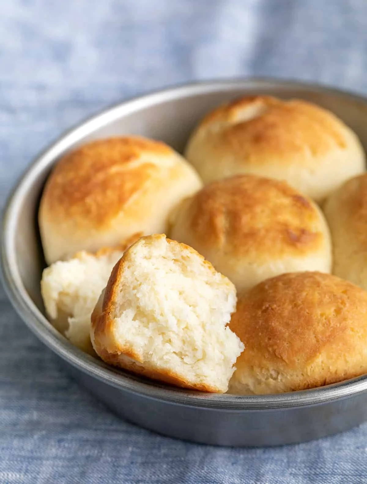 A close up of the finished rolls in a baking tin with one broken in half. 