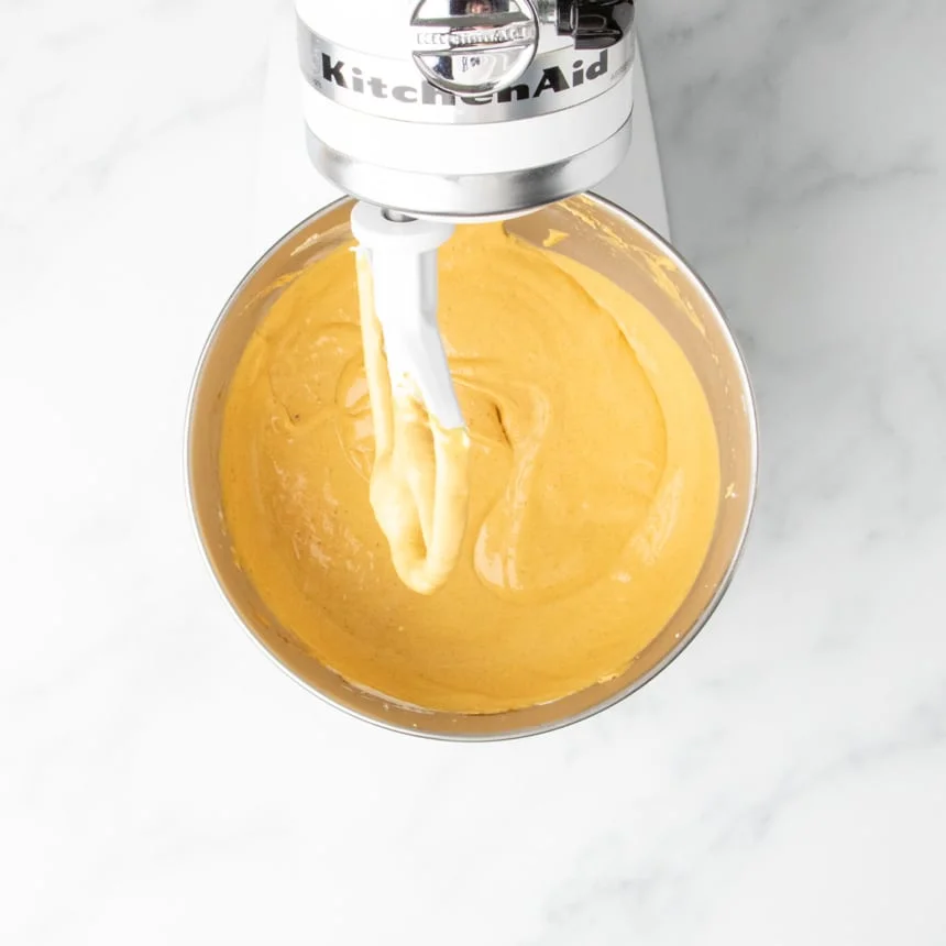 A close-up of the finished, smooth pumpkin cheesecake batter, with eggs beaten in for a somewhat thinner batter, in a stainless steel mixing bowl with the paddle attachment.