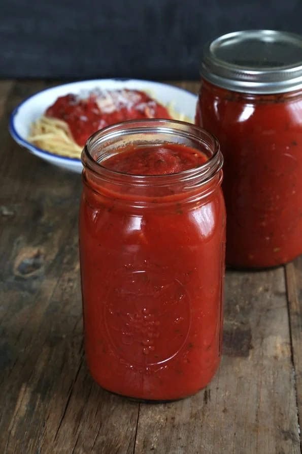 A close up of tomato sauce in jar on wooden surface.