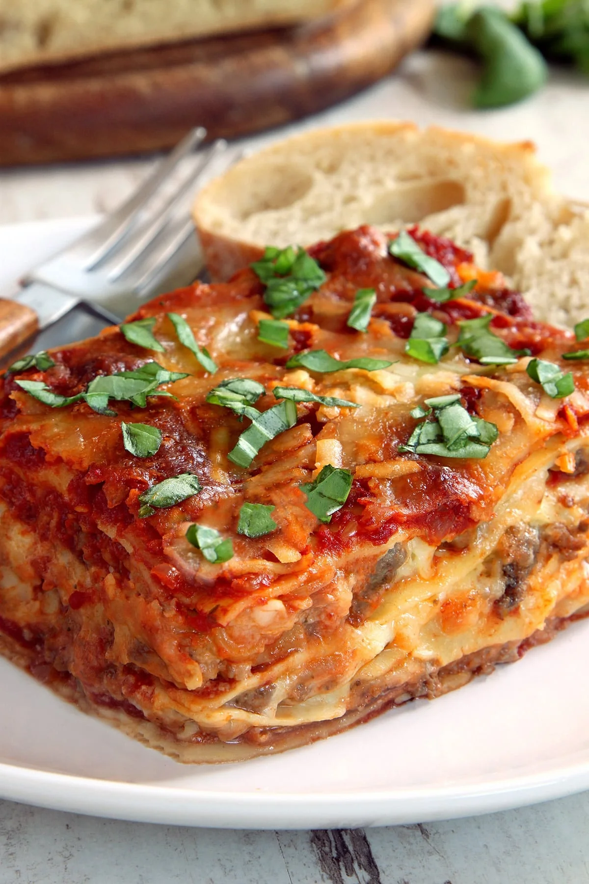 A close up side view of lasagna with herbs on top on a white plate.