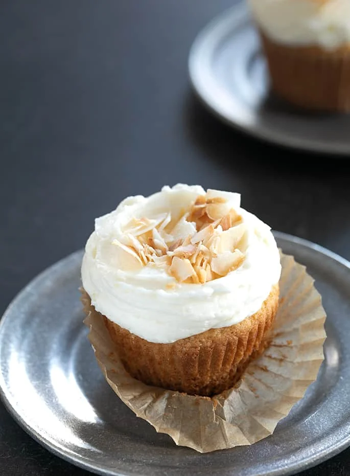 A closeup of a coconut cupcake with frosting and coconut on a small plate