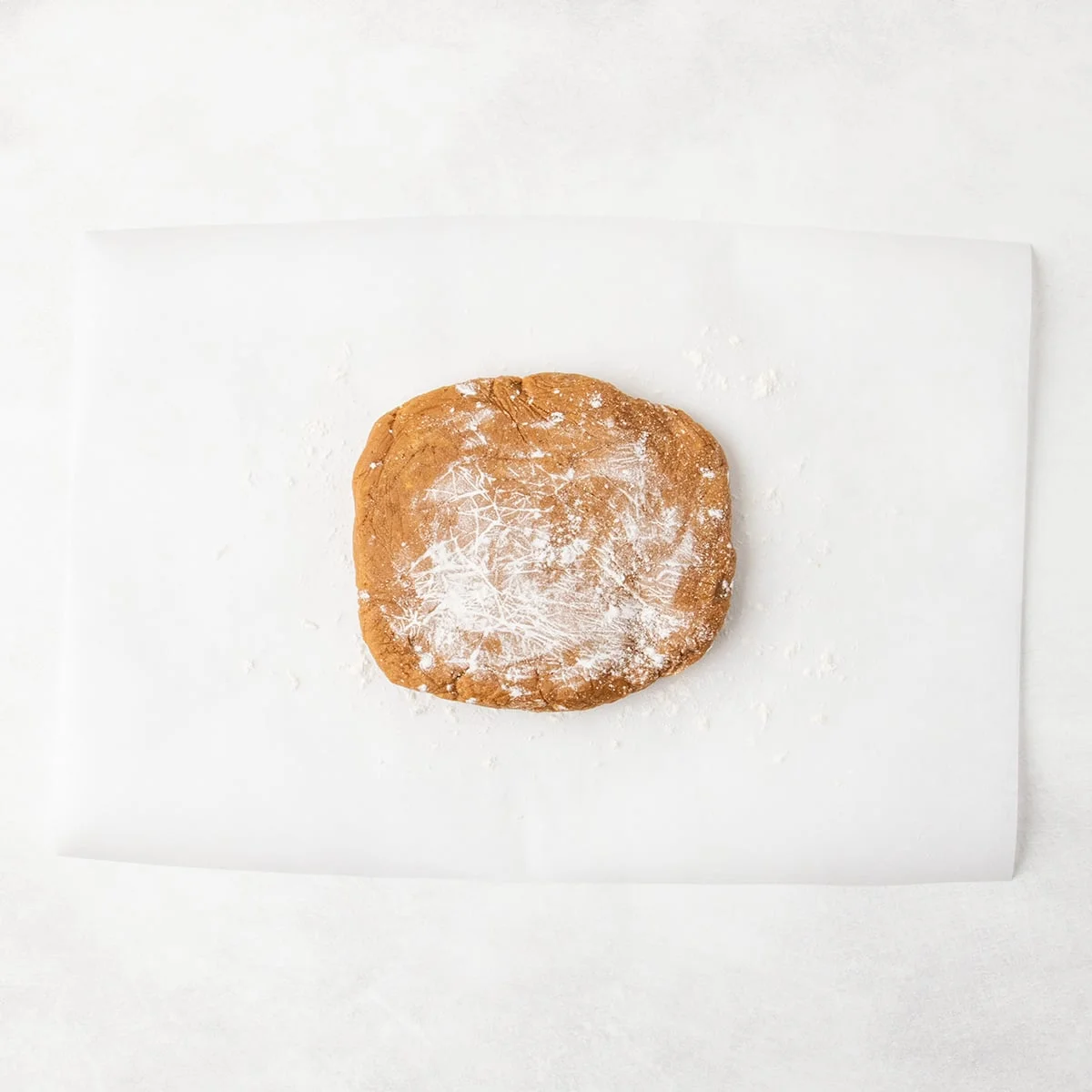 A flattened mound of raw brown cookie dough dusted with flour, placed on a sheet of parchment paper.