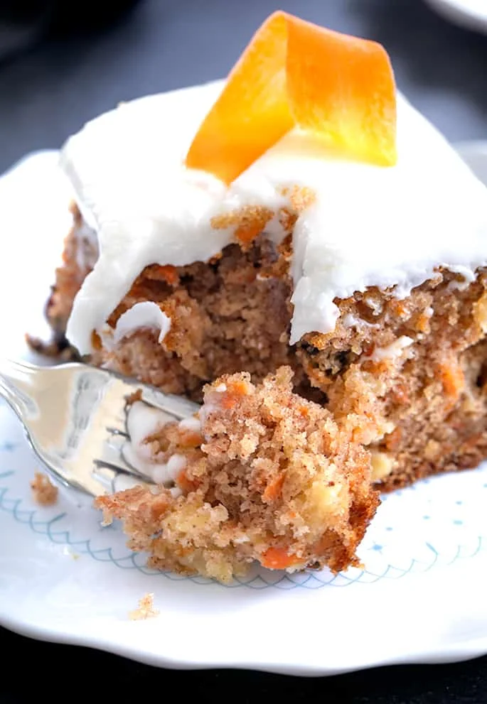 A fork taking a bite from a piece of carrot cake on a plate