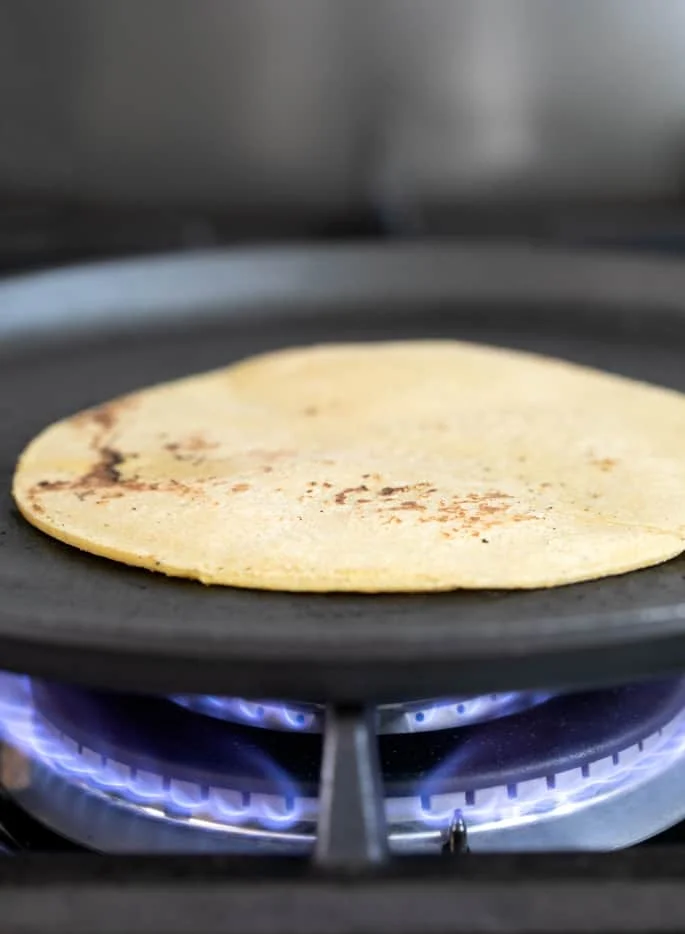 A fresh corn tortilla on a skillet being cooked
