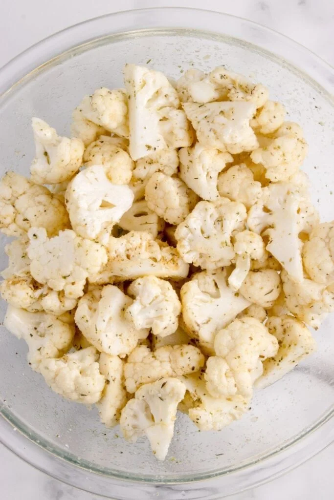A glass bowl with seasoned raw cauliflower in it.