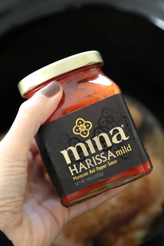 A hand holding a jar of Mina harissa paste.