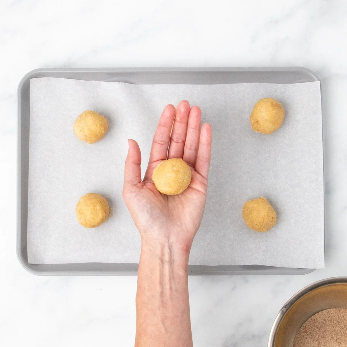 A hand holding one dough ball with more in the background. 