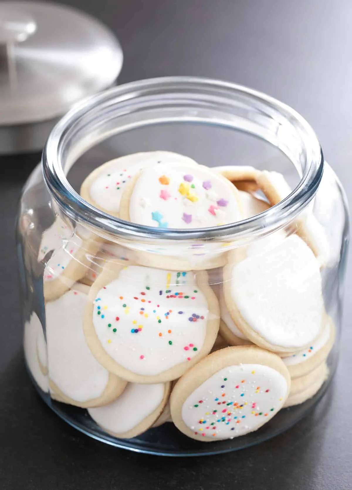 A large glass jar full of round pale cookies with white frosting. 