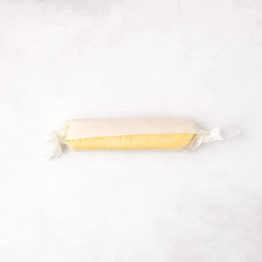 A log of yellow dough wrapped in parchment paper with the ends twisted closed.