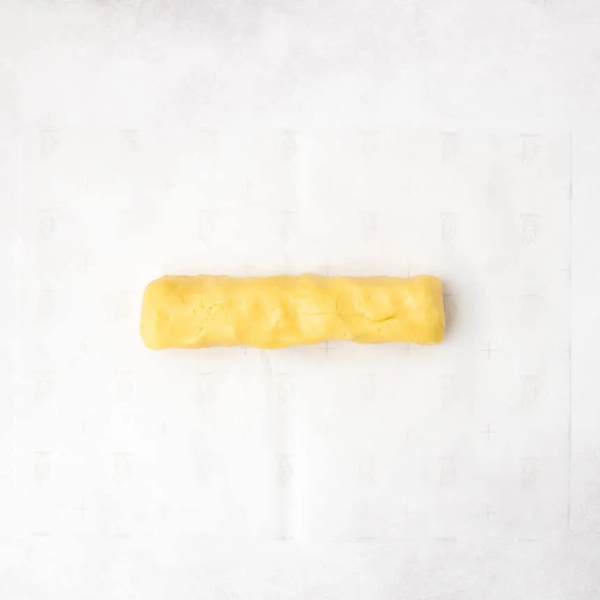 A long, even log of yellow dough resting on a sheet of parchment paper.