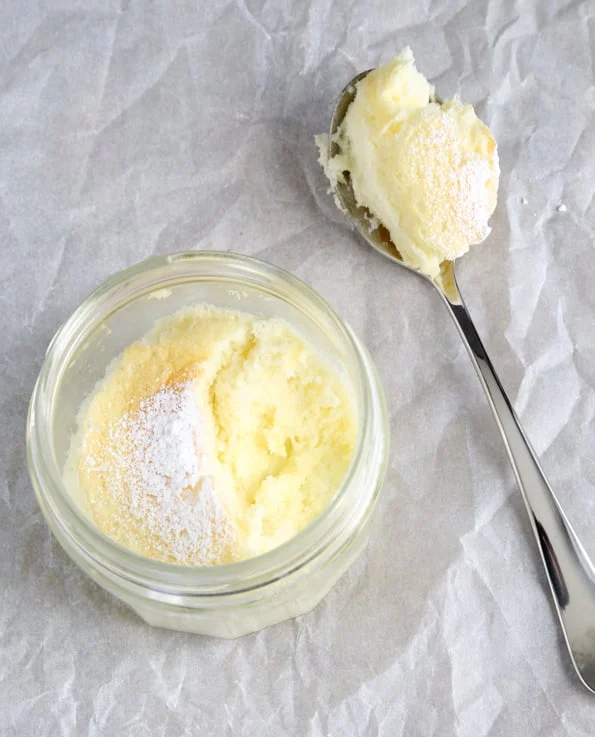 A miniature lemon cake in a jar with powdered sugar and a spoonful taken