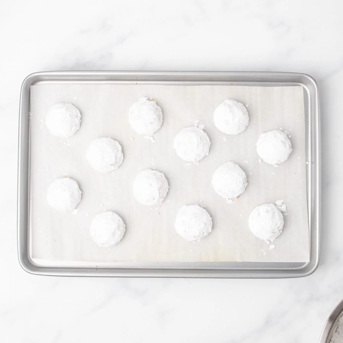 A parchment-lined baking sheet with twelve evenly spaced gluten free Mexican wedding cookies fully coated in white confectioners' sugar.