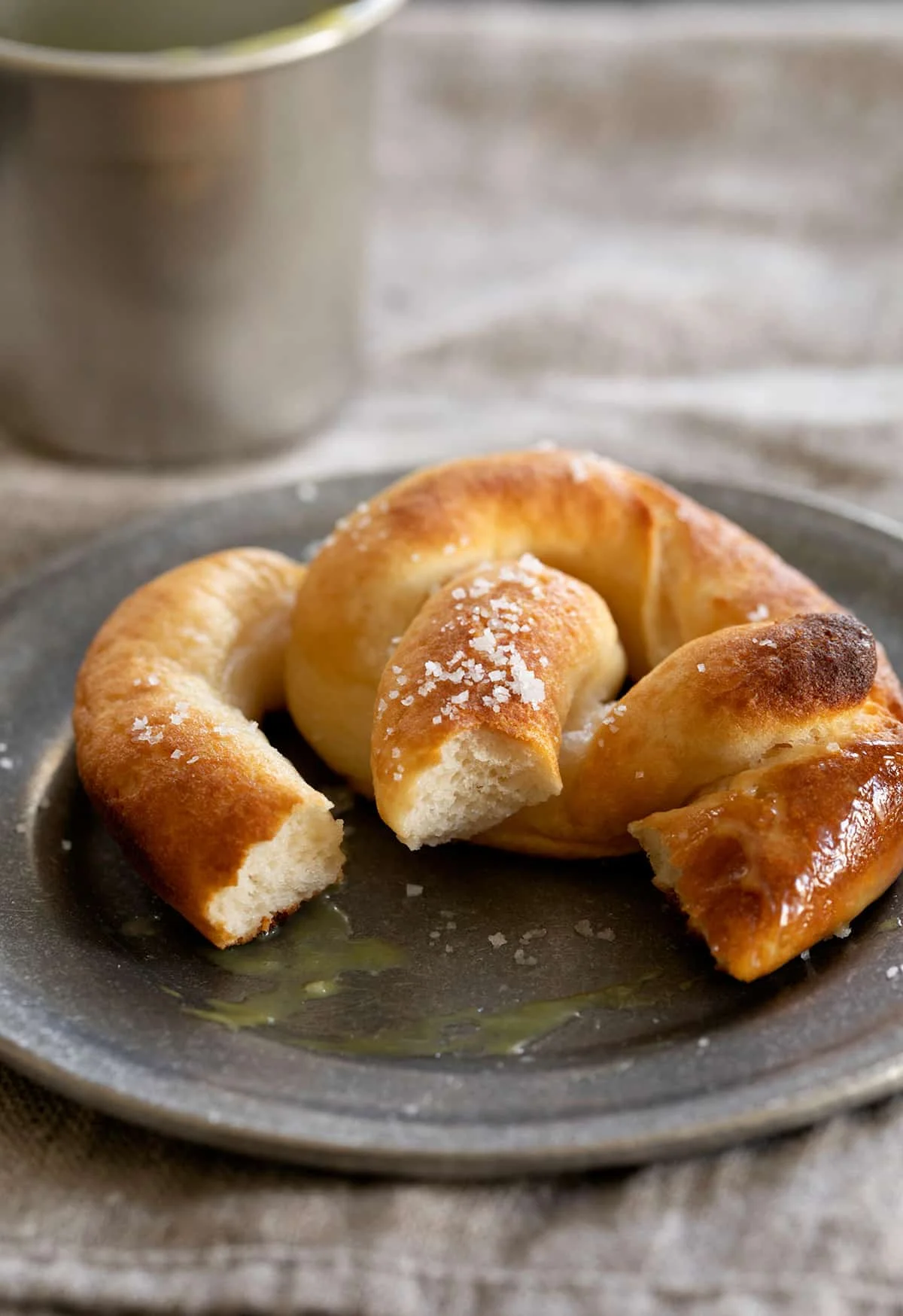 A partially eaten gluten free soft pretzel on a plate with dipping sauce.